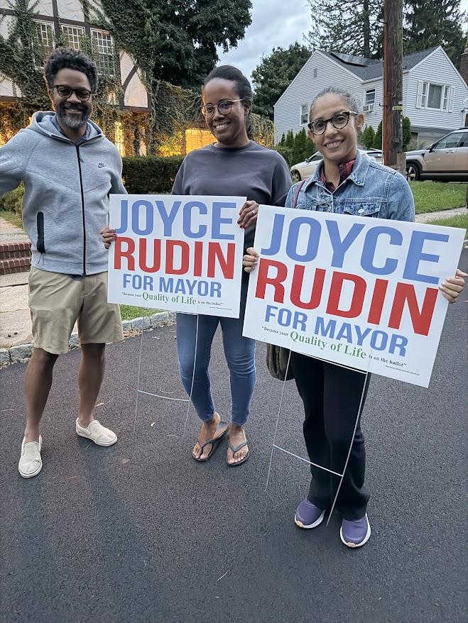 Three supporters holding Joyce Rudin for Mayor lawn signs